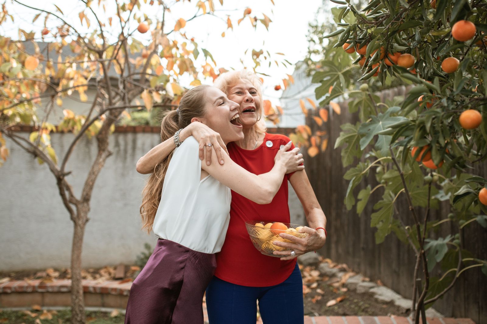 Mum and daughter having a hug while collecting oranges from tree